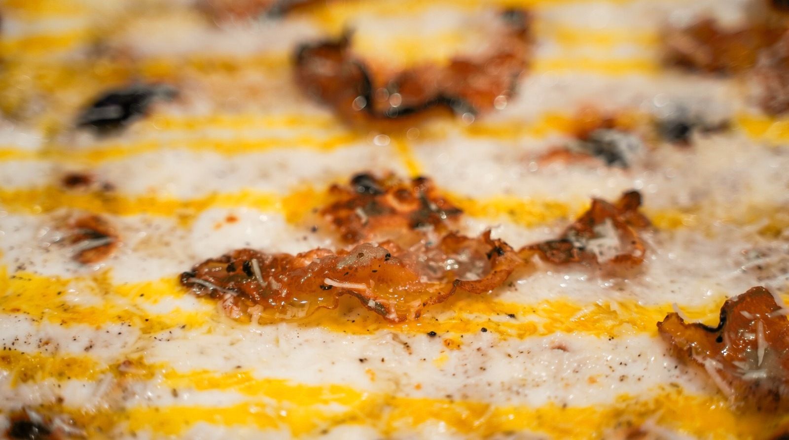 Primo piano di pizza carbonara con tuorlo e guanciale croccante