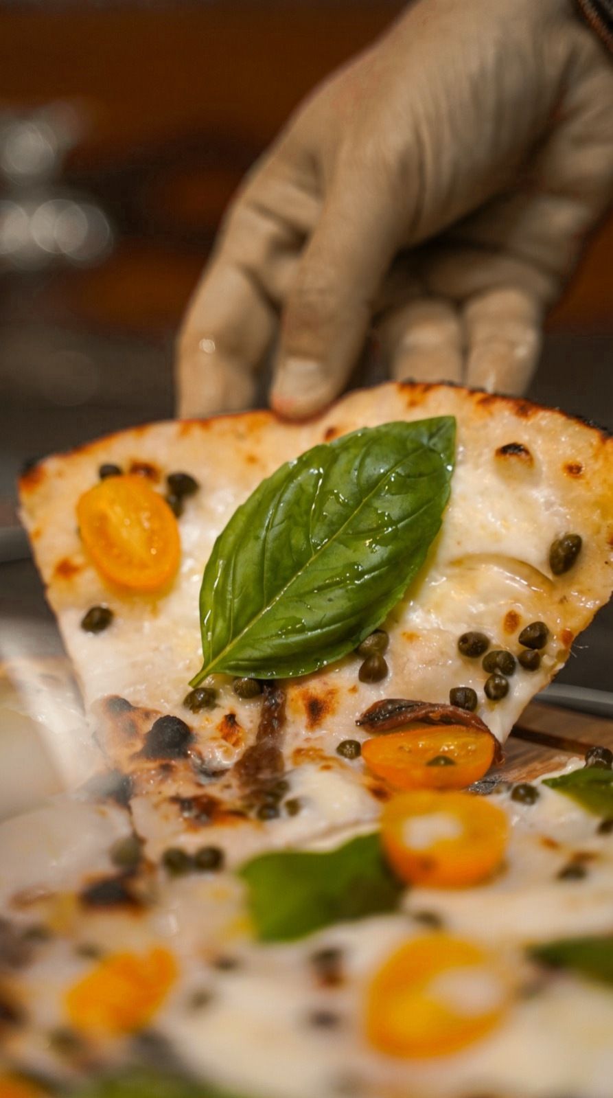 Fetta di pizza bianca con basilico, capperi e datterini gialli